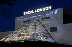 Modern exterior of ExCeL London at night featuring the illuminated glass pyramid entrance and Royal Docks skyline - My London Transfer